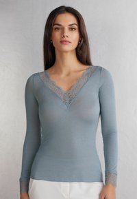 Svetle modré dlouhé rukávy tričko s krajkovým výstřihem do V a krajkovými detaily na manžetách, vyrobené z měkké, průhledné látky.
