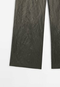 Pantalon ample vert olive foncé avec une texture subtilement froissée, posé à plat sur un fond blanc.