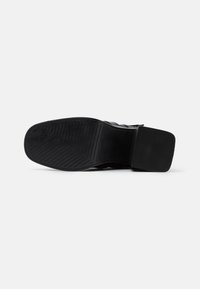 Suela de zapato negra con un patrón texturizado y estriado, y un tacón plano. Presenta un acabado suave y está hecha de material de goma resistente.
