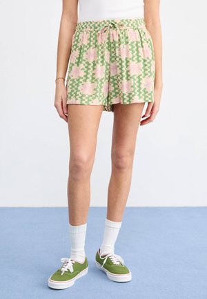 Zöld virágmintás rövidnadrág rózsaszín virágokkal és hullámos mintákkal, rugalmas derékkal és zsinórral, zöld sneakerrel és fehér zoknival párosítva.