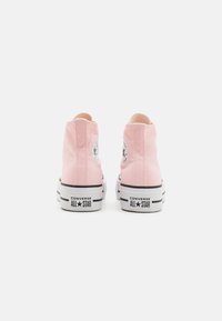 Pink high-top sneakers with canvas upper, white rubber sole, and black accents. Features a circular logo patch on each side.