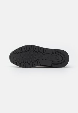 Black rubber sneaker sole featuring a textured surface with circular patterns and ridges. Logo "Reebok" embossed on the side.