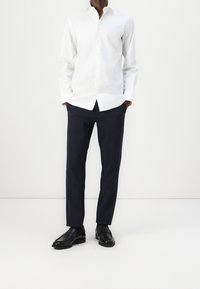 Witte langwerpige overhemd met knopen, gecombineerd met marineblauwe pinstriped broek en zwarte nette schoenen, met een strak ontwerp en een soepele textuur.