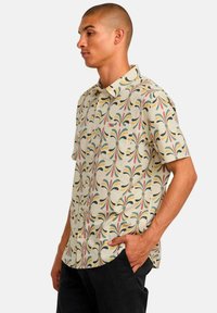 Short-sleeve button-up shirt in light beige with a colorful floral pattern. Features a chest pocket and a relaxed fit. Cotton material.