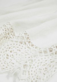 Tissu blanc avec une bordure en dentelle fine comportant des motifs géométriques et floraux le long du bord.
