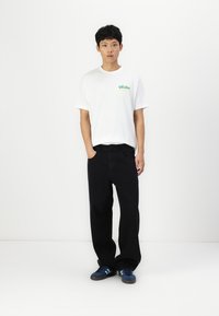 White cotton t-shirt with a colorful "Vacation" logo, paired with relaxed-fit black denim pants and blue sneakers.