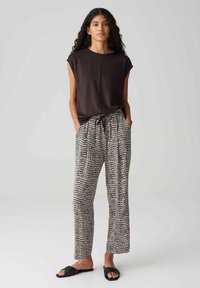 Zwarte top met korte mouwen, gecombineerd met losse zwart-witte gestreepte broek. De broek heeft een trekkoord in de taille en zakken.