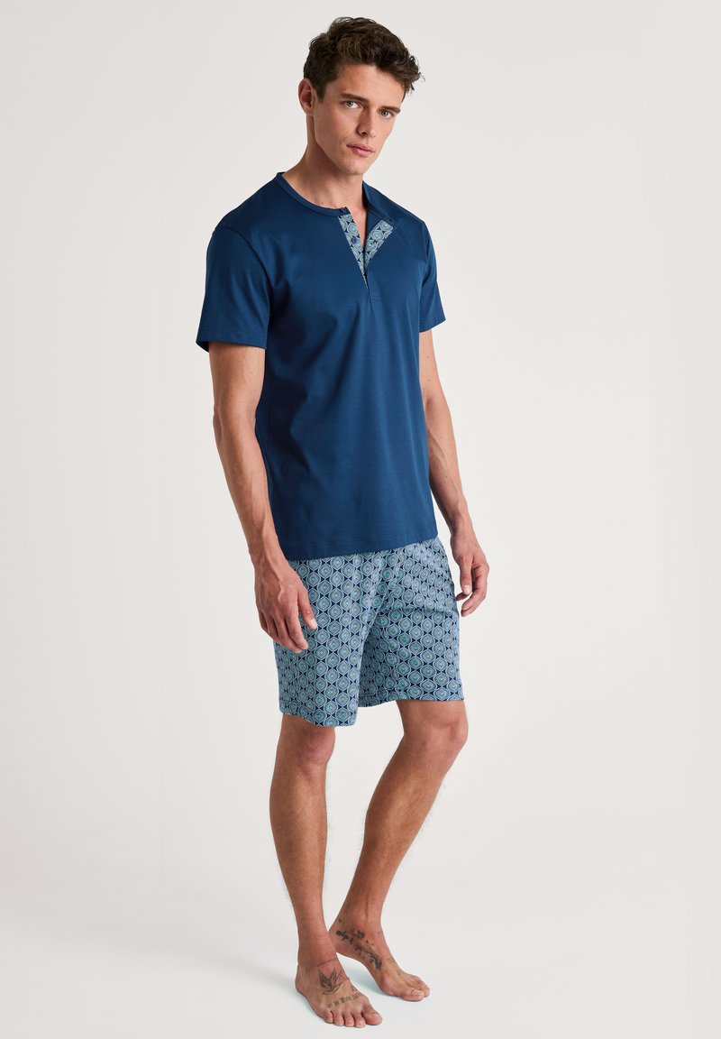 Navyblauw overhemd met korte mouwen en een gestippelde kraag, gecombineerd met blauwe shorts met een patroon van cirkels, beide gemaakt van lichte stof.