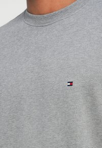 Felpa grigia in cotone con collo rotondo, caratterizzata da un piccolo logo in rosso, bianco e blu sulla parte sinistra del petto.