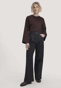 Blusa di cotone color bordeaux con maniche lunghe a campana e chiusura con bottoni. Pantaloni a gamba larga in denim scuro a vita alta. Scarpe basse marroni con frange.
