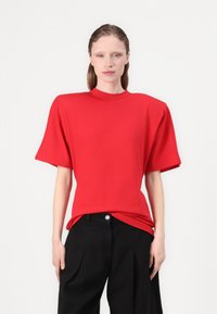 Rode oversized t-shirt met korte mouwen, hoge halslijn en gladde stof. Gecombineerd met zwarte wijde broek. Eenvoudig, modern ontwerp.