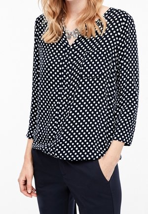 Granatowa bluzka w groszki z długimi rękawami, dekoltem w kształcie litery V, kieszenią z przodu oraz marszczeniem. Wykonana z lekkiego materiału o gładkiej fakturze.