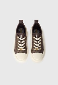 Pruunid lõuendist tennised kreemika kummist varbakatte, kuldsete silmuste ja valgete paeltega. Keelel on logo ning kangas on tekstureeritud.