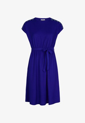 Paarse jurk tot de knie met korte mouwen, een ronde hals en een stoffen ceintuur. Heeft decoratieve stiksels op de schouders.