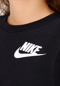 Svart ärmlös träningströja med rund halsringning och en framträdande vit Nike-logotyp på bröstet. Mjuk bomullstyg, avslappnad passform.