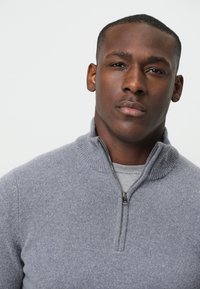 Grauer Reißverschluss-Pullover mit hohem Kragen und gerippten Abschlüssen, aus weichem Strickmaterial gefertigt. Verfügt über einen metallischen Reißverschluss und einen lässigen, geschichteten Look.