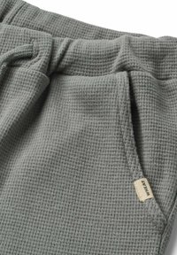 Grau gestrickte Waffelpants mit einem Kordelzugbund, seitlichen Taschen und einem kleinen gewebten Etikett an der Seite.
