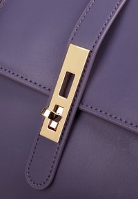 Borsa a tracolla viola in pelle con finitura testurizzata, dotata di una chiusura rettangolare color oro e dettagli di cucitura lungo i bordi.