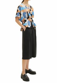 Top colorato e morbido con motivi astratti blu, arancioni e neri. Abbinato a culotte nere a gamba larga e mocassini neri.
