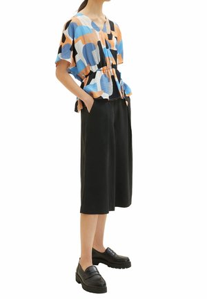 Top colorato e morbido con motivi astratti blu, arancioni e neri. Abbinato a culotte nere a gamba larga e mocassini neri.