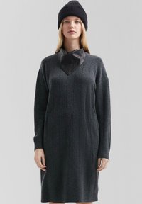 Anthrazitgraues Strickkleid mit langen Ärmeln, rippstrukturiert und mit einem V-förmigen Lederkragen. Kombiniert mit einer schwarzen Strickmütze.