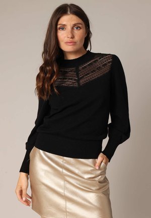 Pull noir avec un panneau de dentelle texturée à l'avant, des poignets et un ourlet côtelés, porté avec une mini-jupe dorée métallisée.