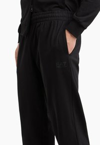Pantaloni jogging neri con vita elastica, tasche laterali e piccolo logo EA7. Tessuto morbido con una consistenza liscia e vestibilità comoda.