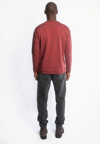 Bordeauxkleurig langemouwen shirt met ronde hals en geribbelde manchetten, gecombineerd met donkergrijze tapered broek en bruine suède laarzen. Achteraanzicht.