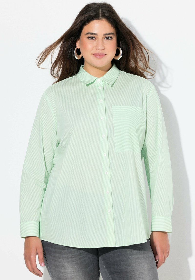 Camicia button-up verde chiaro con righe verticali, maniche lunghe e taschino sul petto. Il tessuto appare liscio con una vestibilità comoda.