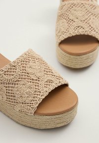 Sandalias de plataforma beige con punta abierta, que cuentan con intrincados patrones florales tejidos y una suela texturizada estilo espadrille.