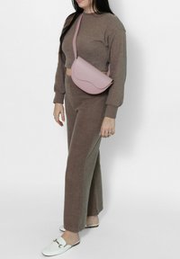 Maglione corto a maglia marrone abbinato a pantaloni larghi coordinati. Una borsa a tracolla rosa chiaro e scarpe slip-on bianche completano il look.