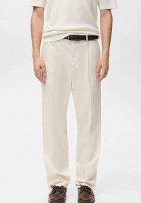 Kremowe spodnie z wysokim stanem o prostym kroju, posiadające przedni zamek, boczne kieszenie i gładką fakturę. Noszone z czarnym paskiem.