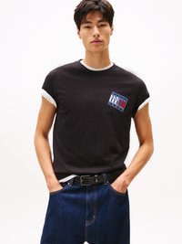Svart kortermet t-skjorte med hvit kant, har et logo-lapp. Kombinert med mørkeblå jeans og et svart belte; uformell passform.
