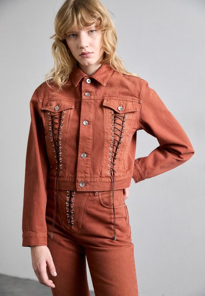 Jachetă din denim de culoare ruginită, croită, cu închidere prin buton, buzunare frontale și detalii cu sfoară pe laterale. Textură netedă cu accente metalice.