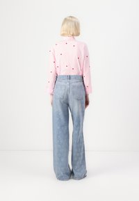 Light pink shirt with red heart prints, paired with high-waisted light blue jeans featuring a heart pattern. Loose fit and long sleeves.