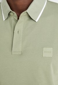 Polo vert avec une finition texturée, comportant un col bordé de blanc et un écusson logo gaufré sur la poitrine.