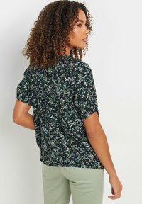 Blusa floral de manga corta, con fondo negro y un estampado de flores en verde, blanco y azul. Fabricada en un tejido ligero y con un corte relajado.