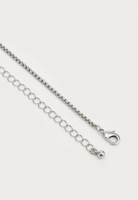 Bracelet en chaîne en métal argenté avec un fermoir en forme de homard, des sections circulaires entrelacées et une finition lisse avec une texture polie.