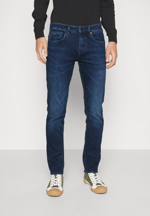 Mörkblå denimjeans med en figurnära design, femficksmodell och kontrasterande sömmar. Kombineras med vita och olivgröna sneakers.