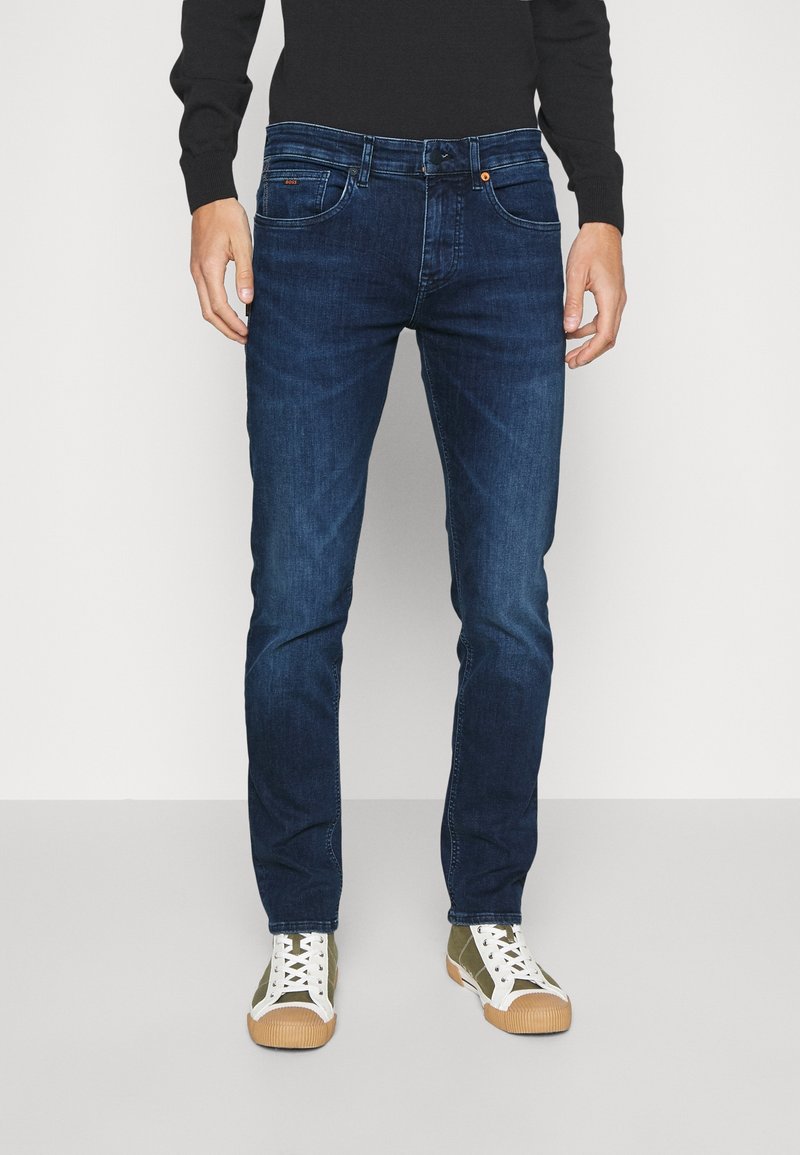 Mörkblå denimjeans med en figurnära design, femficksmodell och kontrasterande sömmar. Kombineras med vita och olivgröna sneakers.