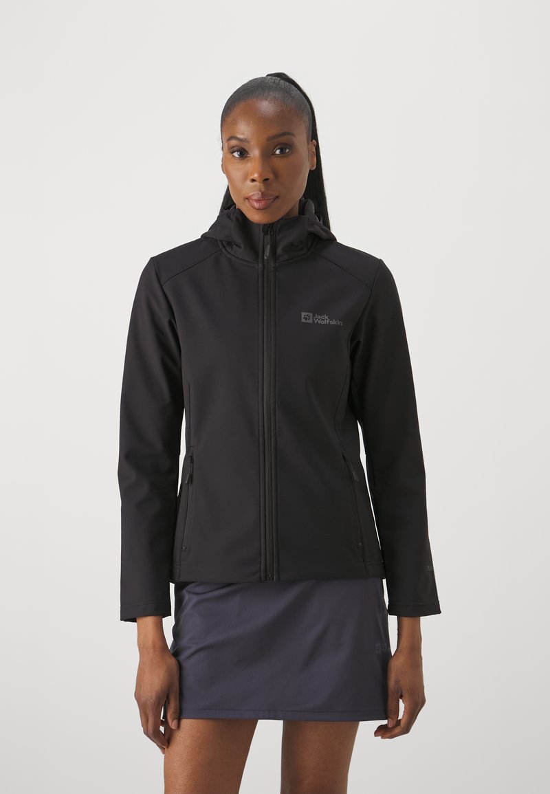 Giacca softshell nera con cappuccio, chiusura a zip frontale, due tasche laterali e dettaglio del logo sul petto, abbinata a una gonna scura. Texture liscia.