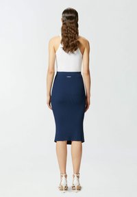 Morska rebrasta midi suknja s prilagođenim krojem, bočnim prorezom i oznakom na struku. Uparena s bijelim sandalama s visokom potpeticom.