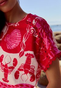 Rød top med et skjell- og hummerprint i pink. Flæser på ærmerne, åndbart stof med en afslappet pasform.