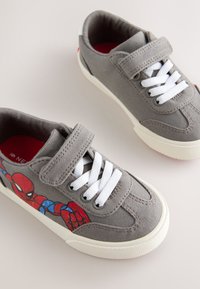 Baskets en toile grise avec un dessin de Spider-Man, lacets blancs et strap en velcro. Semelles en caoutchouc avec motif texturé pour l'adhérence.