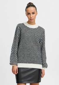 Maglione a righe in bianco e nero con colletto tondo e maniche lunghe; presenta un bordo e dei polsini a costine spessi di colore crema. Abbinato a una gonna in pelle nera.