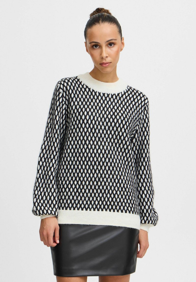 Maglione a righe in bianco e nero con colletto tondo e maniche lunghe; presenta un bordo e dei polsini a costine spessi di colore crema. Abbinato a una gonna in pelle nera.