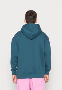 Felpa con cappuccio color verde acqua, dalla vestibilità rilassata, con polsini e orlo a costine, realizzata in tessuto morbido. Presenta un grande cappuccio e dettagli minimal.