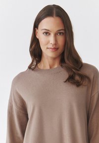 Pull léger marron fabriqué en tissu doux. Présente un large col et de longues manches, avec une coupe décontractée et un ourlet légèrement côtelé.