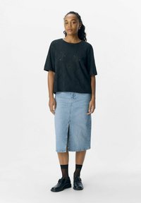 Haut noir à manches courtes avec un motif texturé, associé à une jupe en denim bleu clair avec une fente à l'avant et des chaussures noires à semelles épaisses.