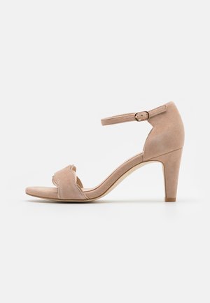 Nackte Wildleder-Sandalette mit High Heel, Knöchelriemen, offenem Zehenbereich und geschwungenem Frontdesign. Verfügt über einen schlanken Absatz und minimalistischen Stil.